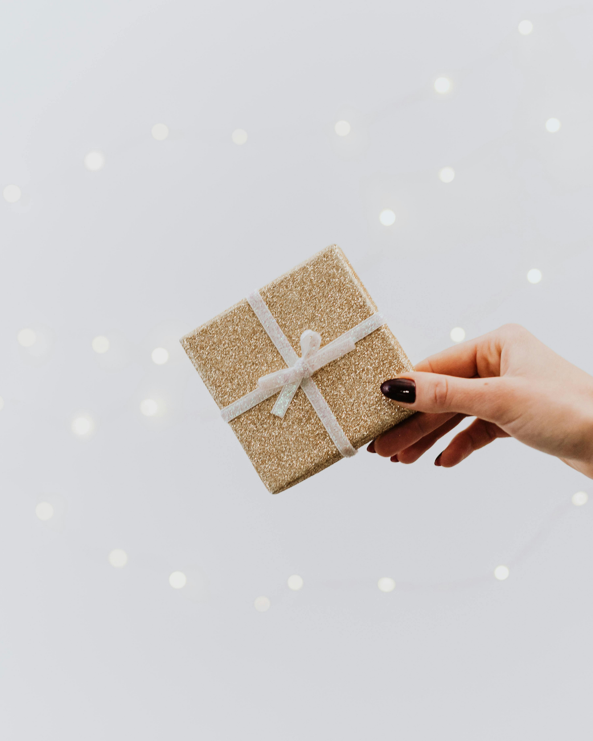Hand holding a small glittery gift box against a light gray background with white dots